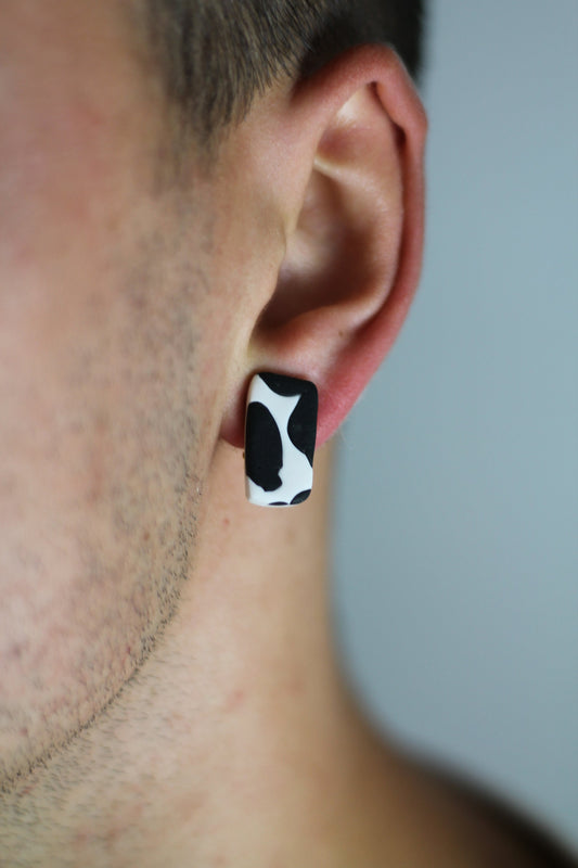 Model wears minimalist earrings in cow print. He also wears handmade hair pins in the shape of a bow.